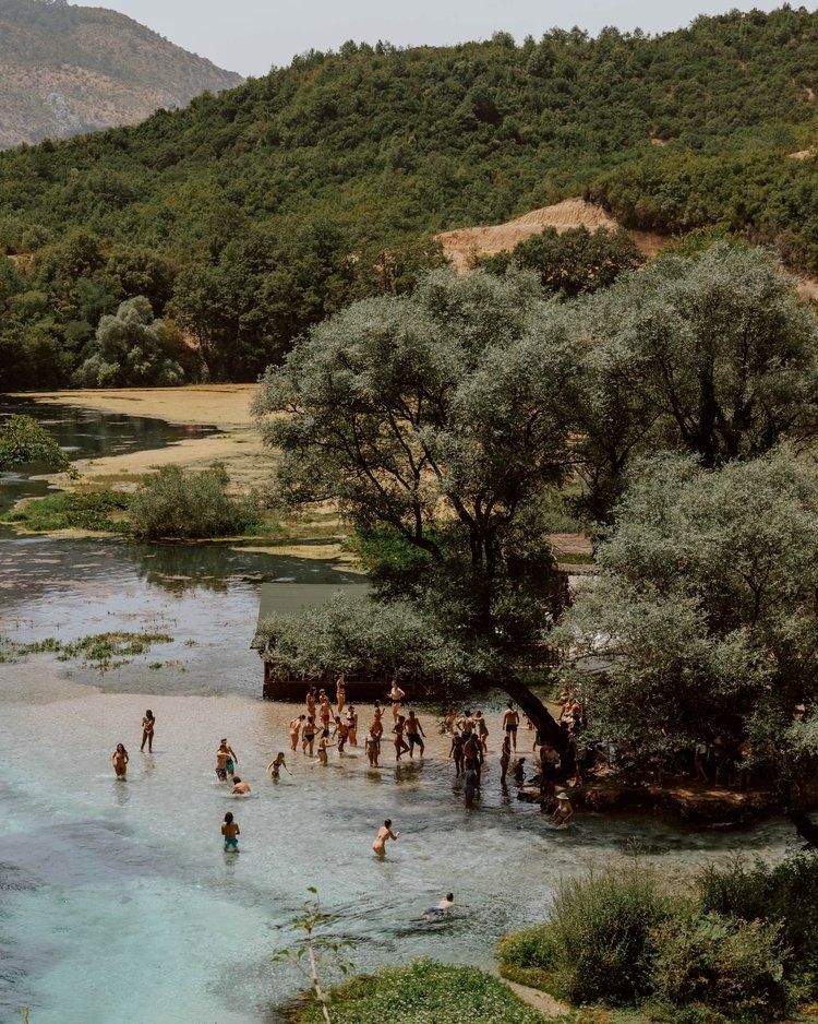 People enjoying clear spring water surrounded by trees in Albania