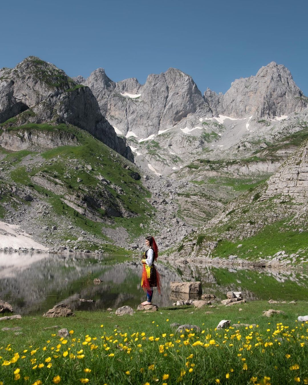 A traveller beside an alpine lake beneath the Albanian Alps