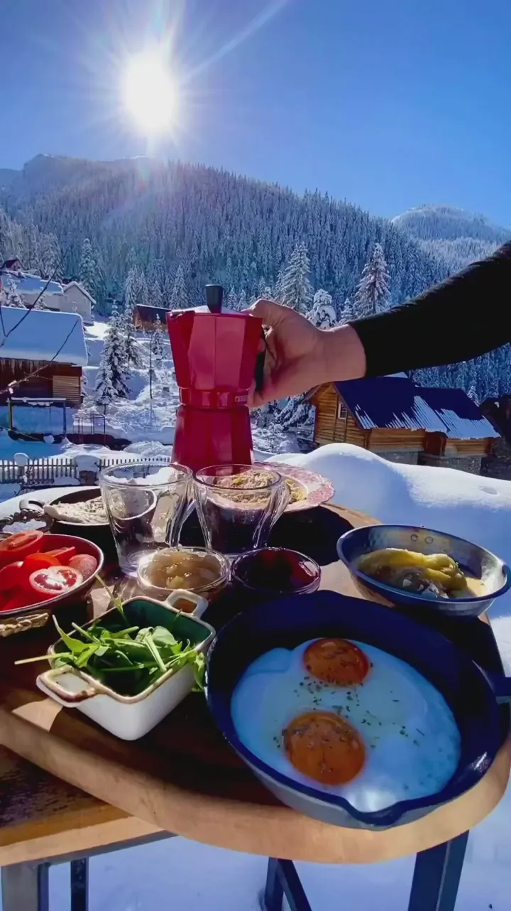 Outdoor breakfast and red coffee pot overlooking snow-covered Albanian mountains